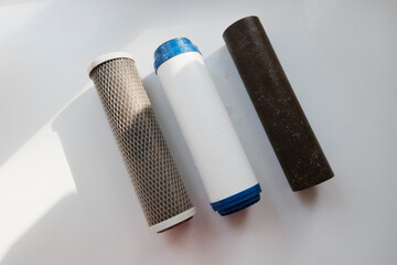 Naklejka premium Electric filter for water purification in the kitchen in the cabinet under the sink. Used dirty filters of varying degrees of purification, three pieces, metal, plastic.