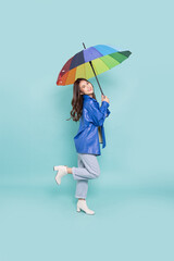 Young Asian woman wearing raincoat and holding rainbow umbrella isolated on green background, In...