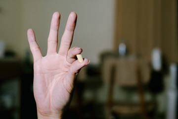 A yellow pill is held by pointing and thumb finger with three other fingers are up. Bokeh or blurred background. Suitable for advertisement.