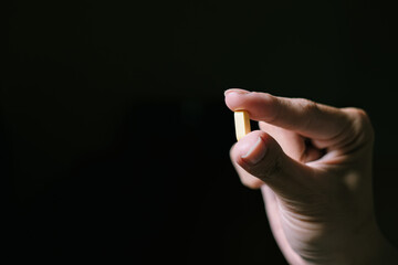 A yellow pill is held by pointing and thumb fingers. Isolated black background. Suitable for...