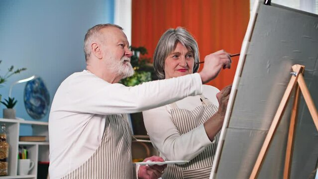 smiling woman and husband are painting a creative picture with brushes and paint on canvas at home