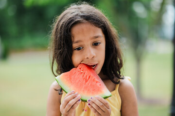 6 year old girl eating watermelon outside on hot summer day