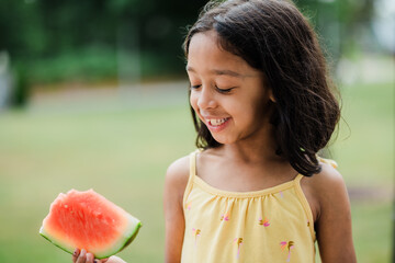 6 year old girl eating watermelon outside on hot summer day