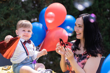 Happy birthday outdoor - A smiling baby wearing Birthday hat celebrates first year with a vibrant party adorned with red and blue balloons and bubble blower and soap bubbles. 