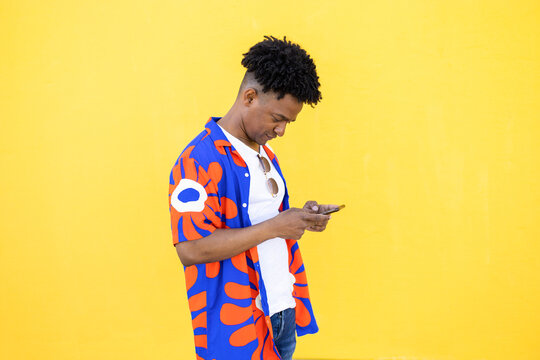 Focused young man using smartphone over yellow background