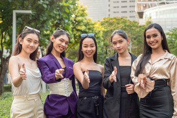 5 friendly and hospitable asian ladies, possibly workmates at the office, offer a handshake. Outdoor scene at the city park.