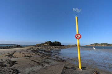 Mermaid spinner and no swimming sign on Yellow post in frond of seascape during low tide in...