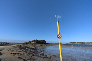 Mermaid spinner and no swimming sign on Yellow post in frond of seascape during low tide in...