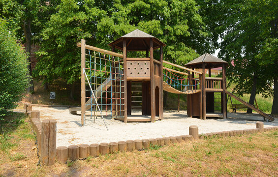 Kids playground construction of wooden huts and climbing net bridge and sand surface ground
