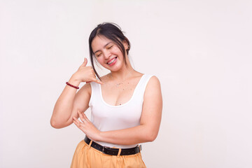 A playful and happy young woman posing with call me gesture and eyes closed. Isolated on a white background.