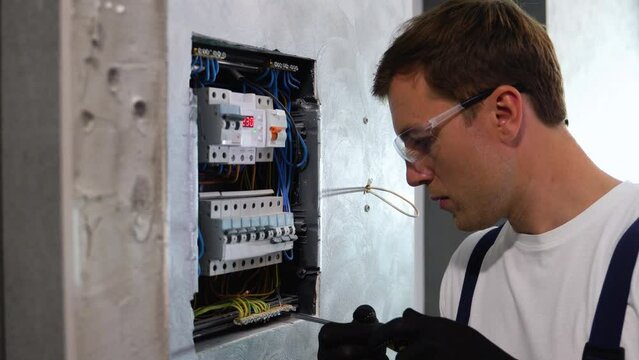 Professional electrician sets up electricity in the apartment. Electrician repairing electrical box and using screwdriver in corridor