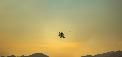 Fototapeta na wymiar Emergency helicopter, firefighters, with the last hours of the sunset sun performing the maneuvers to land on the runway of the Sabadell airport with the mountains and a golden sky on the horizon