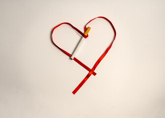 on a white background a red ribbon shaped like a heart with a cigarette threaded through it as if...