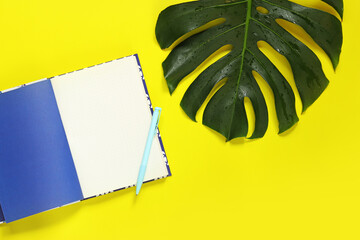 Fototapeta na wymiar Opened notepad, pen and monstera sheet on a yellow background. Notebook, top view. Flat lay, copy space. Place for text