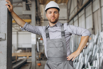 Portrait of a happy worker in a gray uniform and a white hard hat posing on the background of factory production