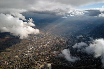 Aerial view from airplane window at high altitude of distant city covered with puffy cumulus clouds...