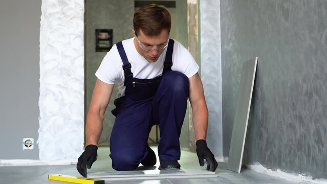 Laying ceramic floor tiles. Worker marking tile to be cut