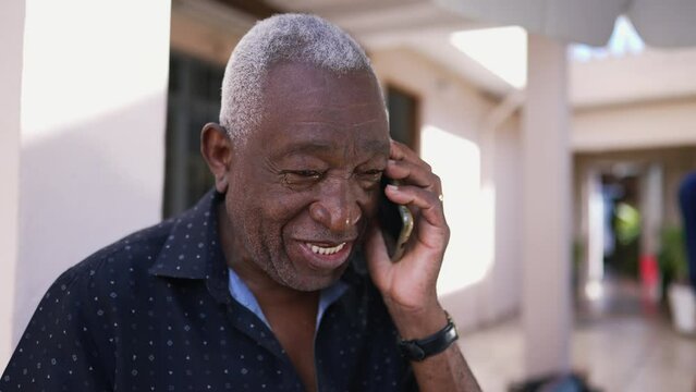 One happy black Brazilian senior man talking on phone outside. Friendly charismatic elderly person using modern technology conversing with smartphone device