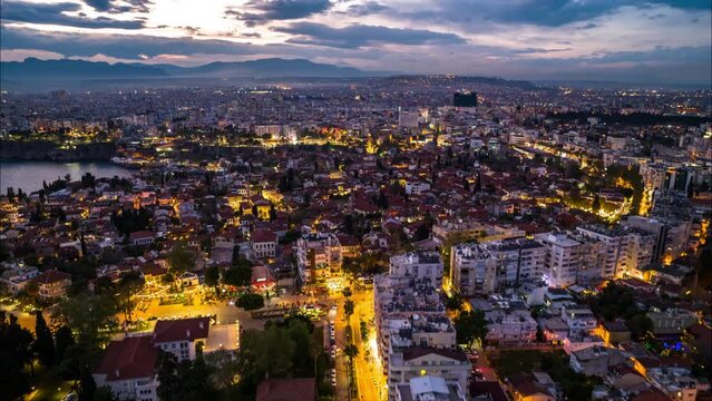 Forwards fly above large city at sunset. aerial hyperlapse shot of illuminated urban neighbourhoods against colourful sky. Antalya, Turkey