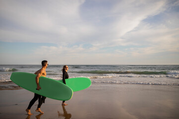 Fototapeta na wymiar Summer Activities. Happy Young Couple Carrying Surfboards Walking Along Shoreline
