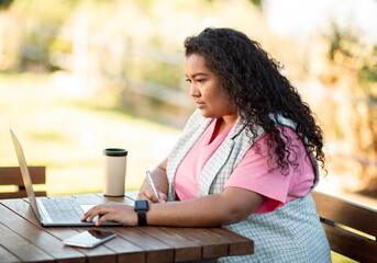 Side view of young hispanic lady typing on laptop outdoors