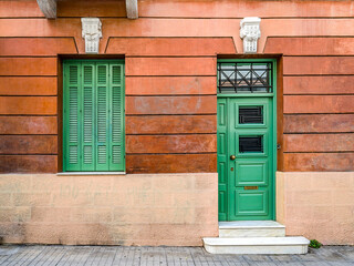 A classic design house facade with a green painted door and window on a dark ocher wall. Travel to Athens, Greece.