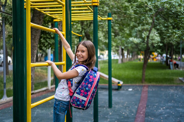 Beautiful school girl with backpack climbing on playground equipment