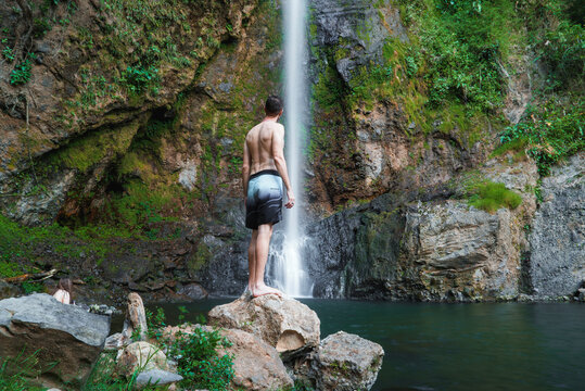 Handsome man in shorts standing on rock admiring gushing waterfall in the rainforest jungle of Costa Rica - Powered by Adobe