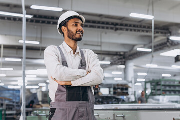 Operator of machine. Industrial Indian international worker indoors in factory. Young technician in white hard hat.