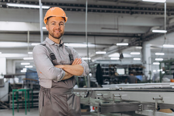Operator of machine. Industrial worker indoors in factory. Young technician in orange hard hat.