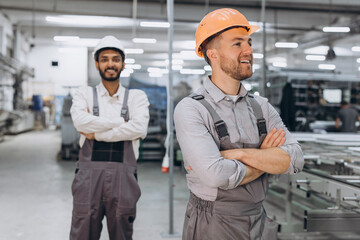 Two international male workers in overalls on the background of the production of PVC windows and doors