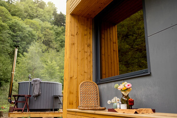 Cozy terrace of a wooden house with hot tub for bathing on background. Recreation in wooden cabins on nature concept