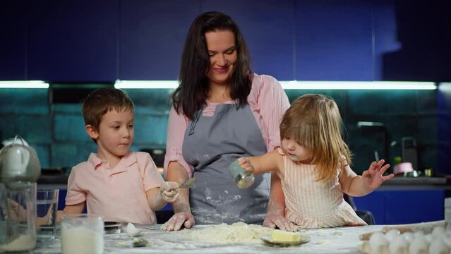 Mother and children add ingredients and salt the dough. The family prepares pastries and cakes at home in the kitchen. High quality 4k footage