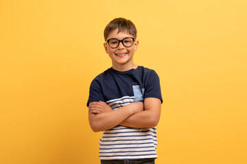 Cheerful school boy wearing eyeglasses posing on yellow background