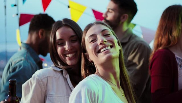 Slow motion. Two young women dancing and having fun with a happy group of best friends at music fest, enjoying and having fun at a party together. Playful people celebrating a weekend night event
