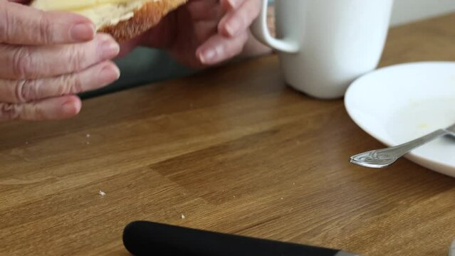 the hands of an elderly Caucasian woman spread bread with butter during a delicious and nutritious breakfast in the family circle.