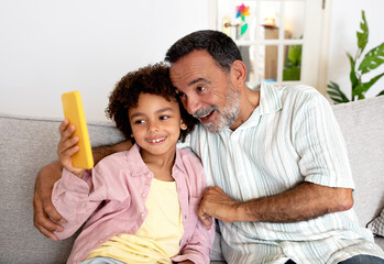 Fototapeta premium Hispanic Grandpa And Grandson Using Cellphone Together At Home