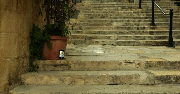 Smartphone with camera app running timer stand on stairs in antique street. Anonymous woman start shutter countdown on phone and run to shoot place to take selfie in touristic place.