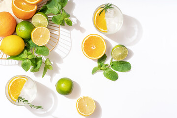 Summer cocktails with citrus fruits orange lemon lime mint and rosemary on a white background. Summer party concept. Trendy palm leaf shadow and sunlight.