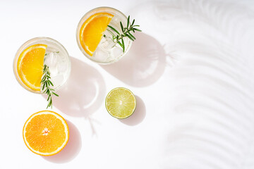 Summer cocktails with citrus fruits orange lemon lime mint and rosemary on a white background. Summer party concept. Trendy palm leaf shadow and sunlight. © Anna