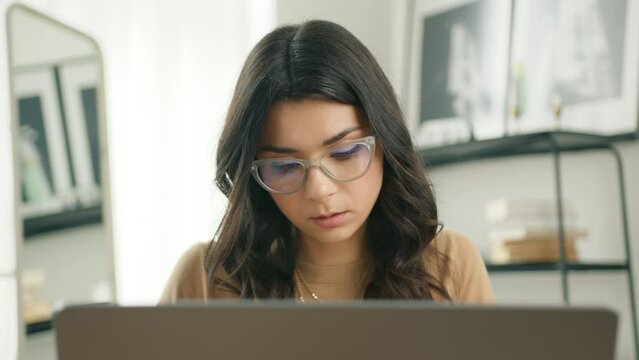 Education concept, smart people portrait slow motion. Hispanic freelancer woman in eyeglasses working on computer. Concentrated latin entrepreneur developing new project while working on laptop home