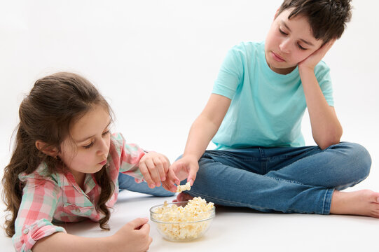 Caucasian happy primary school kids - teenager boy, brother and his younger sister, adorable litttle child girl eating popcorn, isolated on white studio background. Bonding. Family. Lifestyle Leisure