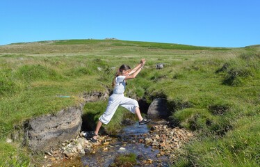 A young girl jumping over a stream in the countryside. 