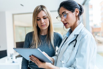 Beautiful female doctor talking while explaining medical treatment with digital tablet to patient in the consultation.