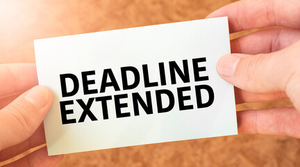 DEADLINE EXTENDED word inscription on white card paper sheet in hands of a businessman. recap...