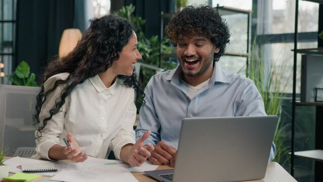 Multiracial business partners multiethnic colleagues Indian businessman and Arabian businesswoman working together paperwork in office happy team celebrate success achievement win startup on laptop