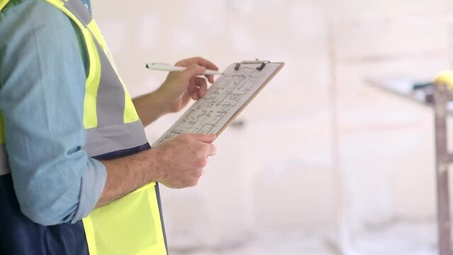 Contractor in vest checking renovation project plan on clipboard worker in professional uniform standing near construction safety equipment in light premise