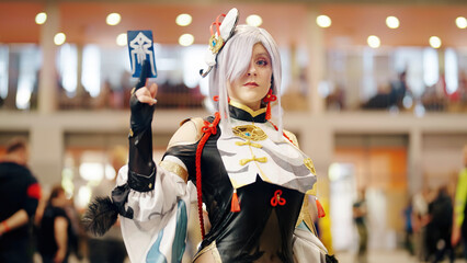 Anime Girl With Gray Hair In Battle Outfit Cosplay Holding Card At The Anime Convention - obrazy, fototapety, plakaty