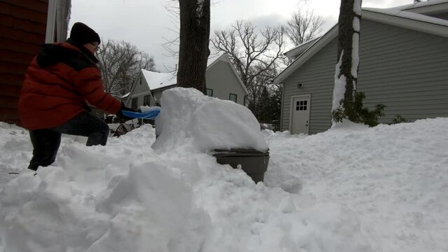 woman digging out trash cans buried in snow after the snow storm