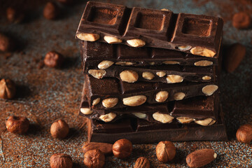 Dark and milk chocolate with nuts on a dark background sprinkled with cocoa powder.
